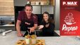 Philipp und Tanja präsentieren in einer modernen Küche zwei Gläser Dalgona-Kaffee mit der charakteristischen cremigen Schaumkrone und Strohhalmen. Vor ihnen auf einem Holzbrett liegen die fertig zubereiteten Dalgona-Zuckerplätzchen zusammen mit einer Stern-Ausstechform.