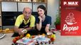 Der Schauspieler Christoph Fälbl und die Patissiere Sarah stehen gut gelaunt in einer modernen Küche. Auf der Arbeitsplatte vor ihnen stehen zwei fertige Früchte-Crumbles in blauen Förmchen, umgeben von frischen Zutaten wie Marillen, Pfirsichen und Beeren.
