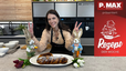 Tanja Pfaffeneder präsentiert lächelnd einen frisch gebackenen, goldbraunen Osterzopf in Hasenform, der mit Puderzucker bestäubt auf einer weißen Servierplatte liegt. Die Szene in der modernen Küche ist passend zum Rezept mit dekorativen Osterhasen-Figuren und bunten Tulpen gestaltet.